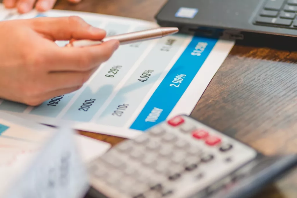 A picture of a sheet of paper with interest rates on it and a hand with a pen in it.